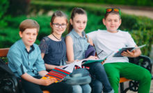 Happy Schoolmates Portrait. Schoolmates seating with books in a wooden bench in a city park and studying on sunny day
